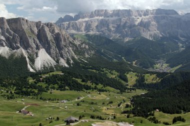 Ortisei, Dolomitler, Güney Tyrol Bölgesi, İtalya 'da bulutlu bir gökyüzüne karşı dağlık bir alan ve küçük kulübelerle manzara fotoğrafı.