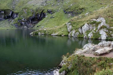 Romanya 'daki Transfagarasan dağ yolunda Balea Gölü' nün pürüzsüz yüzeyi ve yeşil tepeler manzaralı manzara fotoğrafı