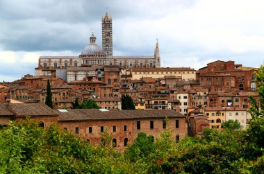 İtalya 'nın Toskana bölgesinde fırtınalı bir gökyüzüne karşı çekilen fotoğrafın ortasında Duomo di Siena ile Siena şehrinin tarihi kısmına bakın.