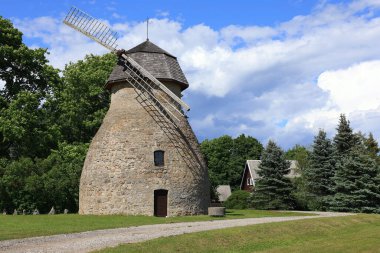Aaspere, Estonya - 09 Temmuz 2024: Bulutlu mavi bir gökyüzüne karşı bir yel değirmeniyle manzara fotoğrafı