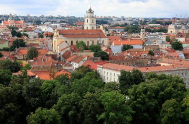 Vilnius (Litvanya) şehrinin tarihsel bölümünün panoramik görüntüsü, fırtınalı bir gökyüzünün arka planında sayısız kilise ve yeşil ağaçlar var.
