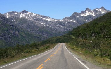 Norveç 'teki Lofoten Adaları' ndaki mavi gökyüzüne karşı yol ve dağ manzaralı bir arabanın manzara fotoğrafı.