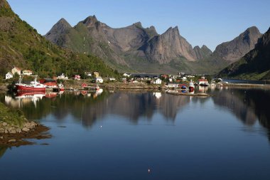 Norveç 'teki Lofoten Adaları' ndaki Reine yakınlarındaki suya yansıyan bir körfez, dağlar, gemiler ve evler manzaralı manzara fotoğrafı.