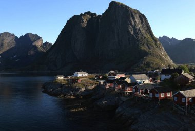 Norveç 'in Lofoten Adaları' ndaki Hamnoy köyünde sabahın erken saatlerinde bir dağ zeminine karşı kırmızı evleri gösteren manzara fotoğrafı.