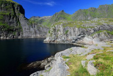 Norveç 'teki Lofoten Adaları' ndaki A köyünde bulutlu mavi gökyüzü manzaralı bir deniz koyunun ve sıradağların olduğu manzara fotoğrafı.