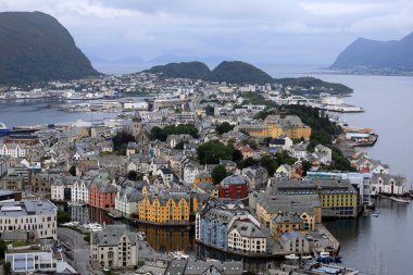 Norveç 'in Alesund şehrinde şafak vakti arkaplanda renkli evler ve dağlar manzaralı panoramik hava fotoğrafı