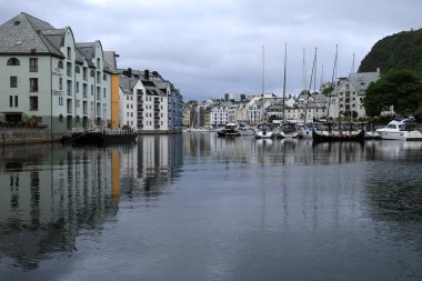 Alesund, Norveç - 17 Temmuz 2024: Rıhtımdaki tarihi binaların görüntüsü gün batımında körfezin suyuna yansıdı.