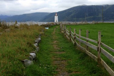 Landscape photo with a view of the mountains, the sea, the Hogsteinen lighthouse and the path leading to it, in the morning in the village of Godoya, near Alesund in Norway