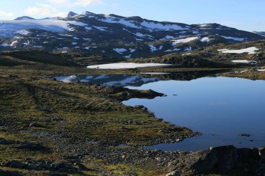 Norveç 'te Lm yakınlarındaki Sognefjell Yolu' nda sabahın erken saatlerinde Fantesteinsvatnet Gölü ve karla kaplı dağları gösteren manzara fotoğrafı.