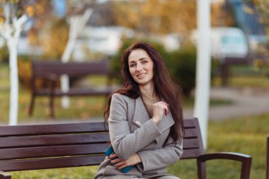 Parkta çimlerde oturan bir kadın dizüstü bilgisayarla çalışıyor. Kulaklık takan bir kadın parkta bir ağacın altında otururken dizüstü bilgisayar kullanıyor. Arkasından parlak güneş ışığı geliyor. Yüksek kalite fotoğraf