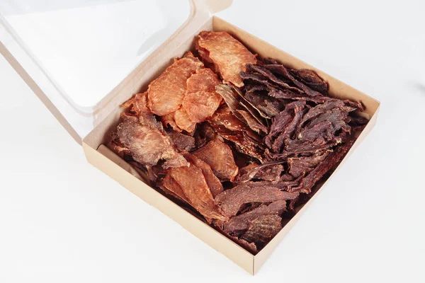 Some craft cardboard boxes with dehydrated dog treats, the highest one is opened, full of dry meat crunchy tastes from beef and chicken. Homemade pet food, healthy and natural. Copy space. High quality photo