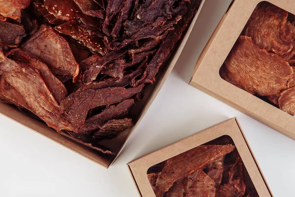 Some craft cardboard boxes with dehydrated dog treats, the highest one is opened, full of dry meat crunchy tastes from beef and chicken. Homemade pet food, healthy and natural. Copy space. High