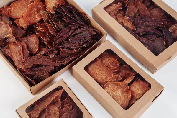 Some craft cardboard boxes with dehydrated dog treats, the highest one is opened, full of dry meat crunchy tastes from beef and chicken. Homemade pet food, healthy and natural. Copy space. High