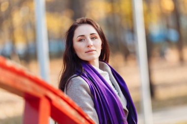 Uzun saçlı genç bir kadının portresi güneşli bir sonbahar gününde temiz hava soluyan gri bir palto ve mor bir eşarp giyen. Yüksek kalite fotoğraf