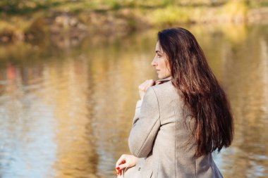 Uzun saçlı genç bir kadının portresi güneşli bir sonbahar gününde temiz hava soluyan gri bir palto ve mor bir eşarp giyen. Yüksek kalite fotoğraf