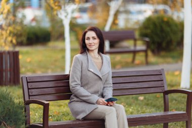 Parkta çimlerde oturan bir kadın dizüstü bilgisayarla çalışıyor. Kulaklık takan bir kadın parkta bir ağacın altında otururken dizüstü bilgisayar kullanıyor. Arkasından parlak güneş ışığı geliyor. Yüksek kalite fotoğraf