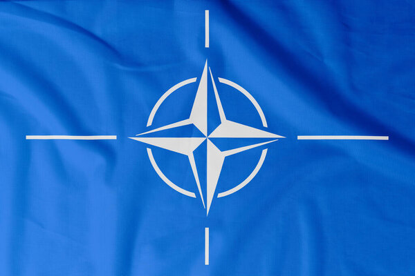 Флаг Организации Североатлантического договора (НАТО) с естественными материальными складками в качестве фона