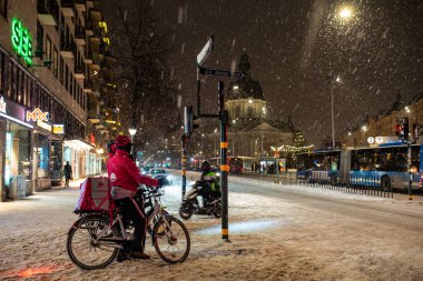 Stockholm, Sweden - January 06, 2023: Foodora food couriers on bicycles at Odenplan during harsh snowfall