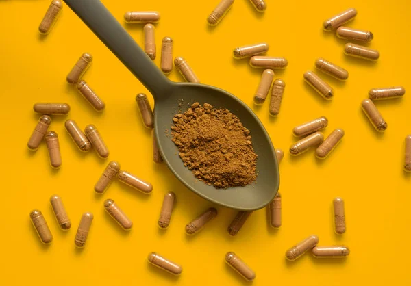 Kratom dolu kaşık ile turuncu zemin üzerinde kratom hapları bileşimi, üst görünüm, düz uzanma