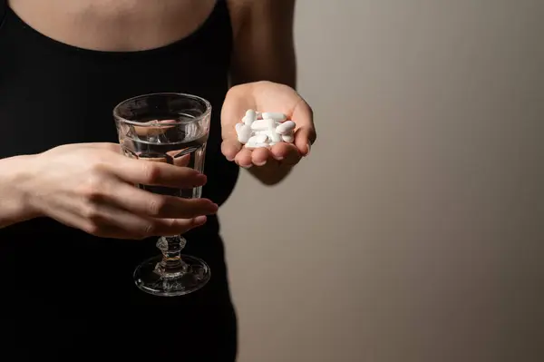 Self help medication concept: woman holds glass of water and a pill to kill the pain, prescribed supplement medication
