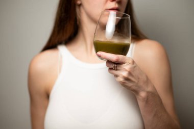 Kratom tüketim konsepti: dişi bir bardak yeşil sıvı içmeye hazır, sıcak suda eritilmiş kratom tozu, kratom çayı, yakın çekim fotoğrafı, seçici odak