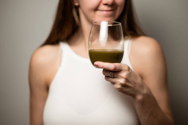 Kratom tüketim konsepti: dişi bir bardak yeşil sıvı içmeye hazır, sıcak suda eritilmiş kratom tozu, kratom çayı, yakın çekim fotoğrafı, seçici odak