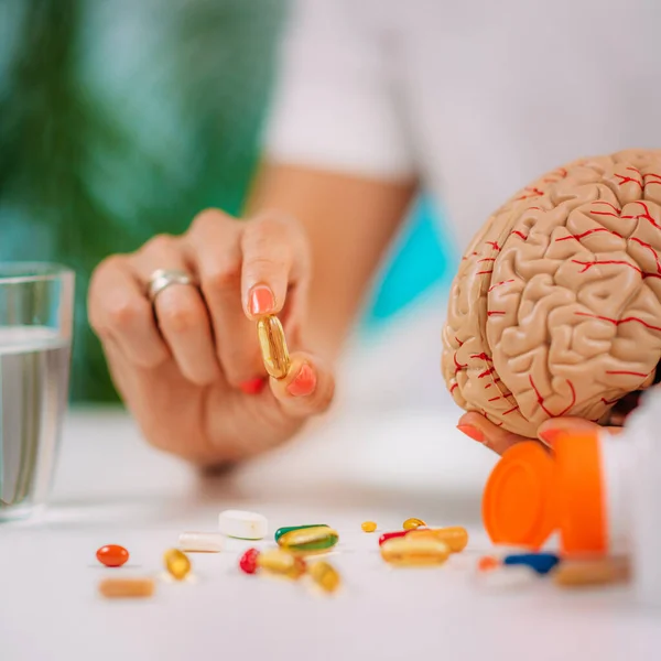 stock image Cognitive improvement or brain supplements. Woman holding a supplement capsule and a model brain.