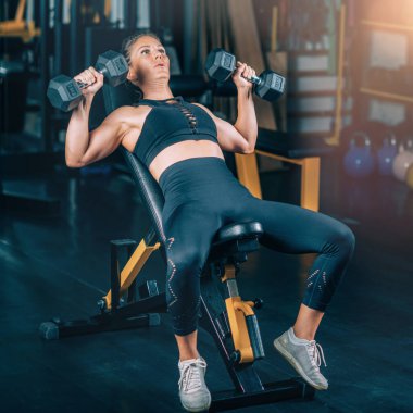 Spor salonunda Dambıllarla egzersiz yapan bayan sporcu. Kuvvet Eğitimi.