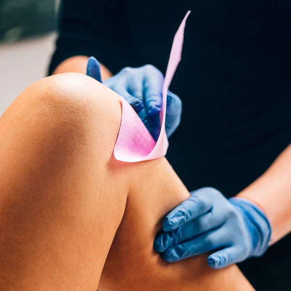 Waxing Kosmetikerin Entfernt Unerwünschte Haare Vom Weiblichen Bein Mit Wachsstreifen — Stockfoto