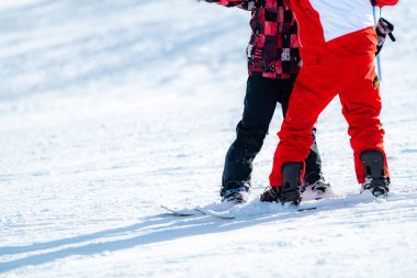 Bir eğitmenle Snowboard sürmeyi öğrenen çocuk.