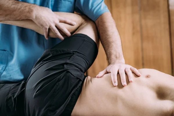 Physical therapist massaging injured leg of a male athlete. Sports injury physical therapy treatment.