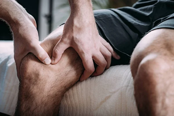 Physical therapist massaging injured knees of a male athlete. Sports injury physical therapy treatment.