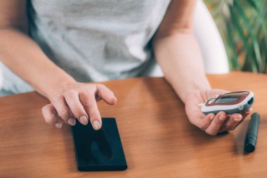 Üst düzey kadın kan şekeri seviyesini ölçüyor. Sonuçları takip etmek için akıllı telefon kullanıyor.