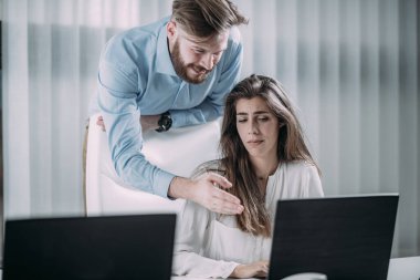 İş yerinde baskı var. Genç hırslı erkek patron baskı altında genç bayan çalışanın arkasında duruyor. Psikolojik taciz..