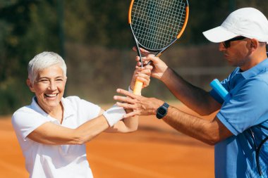 Tenis eğitmeni yaşlı kadına tenis oynamayı öğretiyor.