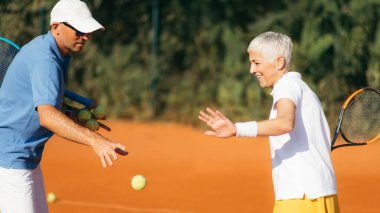 Eğitmenle tenis antrenmanı yapan aktif kıdemli kadın. 