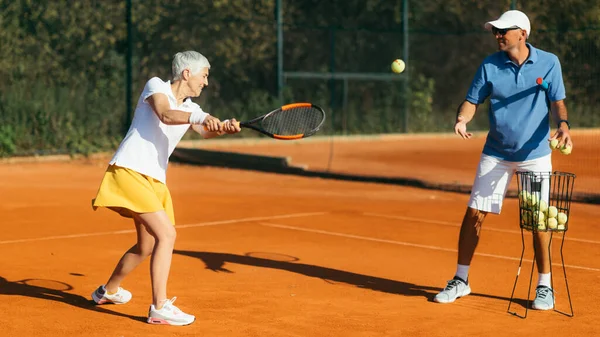 积极的资深女子与教练练习网球 — 图库照片