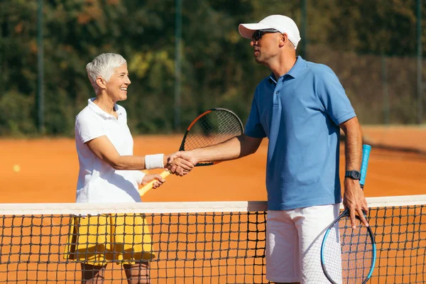 在泥场上上网球课后与60多岁的老妇人握手的网球教练 — 图库照片