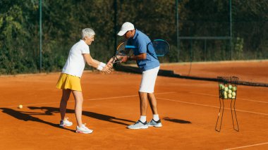 Eğitmenle tenis antrenmanı yapan aktif kıdemli kadın.  
