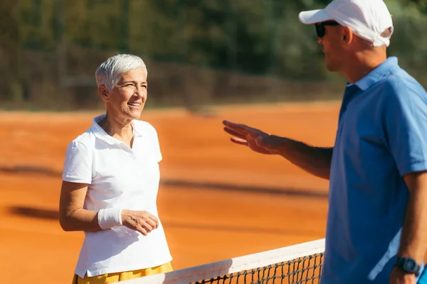 六十岁高龄女子网球教练 在泥场上上网球课 — 图库照片