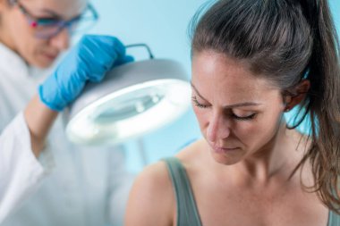 Dermatoloji cilt incelemesi. Yetenekli bir cildiyeci, bir kadın hastanın cildini kişisel bakım ve cilt tazelemesi için değerlendirir..  