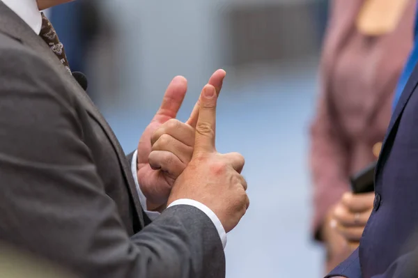 A businessman uses his hands to explain complex concepts to a group of attendees at a trade show. His engaging presentation helps to attract a crowd and showcase his knowledge and expertise.