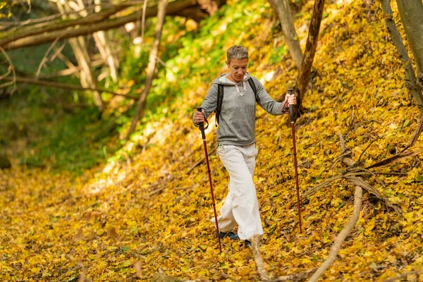 Mindful forest hike. Sporty middle-aged woman, hiking the forest trails, enjoying her surroundings on a beautiful autumn day, feeling harmony with nature