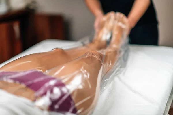 Anti-cellulite vacuum slimming treatment with a nylon bag for legs. Female client lying on a massage table in a beauty wellness center.