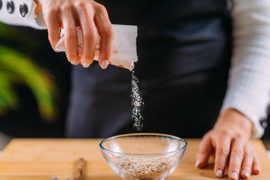 Kadın yulaf ezmesi yapmak için kaseye yulaf ekliyor.