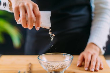 Kadın yulaf ezmesi yapmak için kaseye yulaf ekliyor.