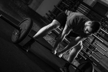 Ağır halterleri kaldırarak kendini adamış erkek sporcu, gücü ve kararlılığı sembolize ediyor, siyah ve beyaz fotoğraf