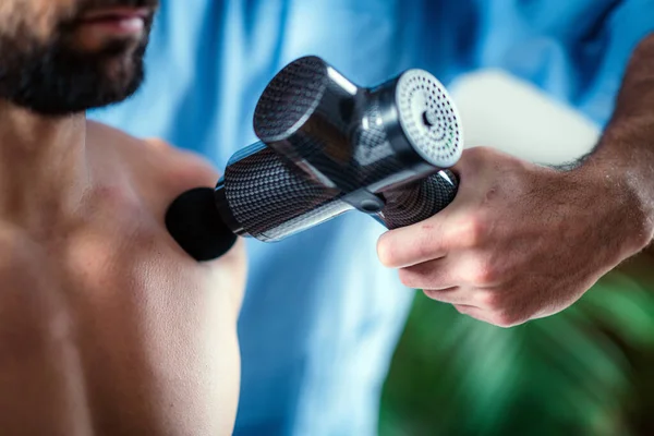 Therapist Treating Injury on Mans Shoulder with Massage Gun