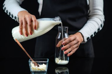 Kadın cam şişeye kefir kültürü tanecikleriyle süt dökerek ev yapımı kefir yapıyor. Siyah arkaplan.