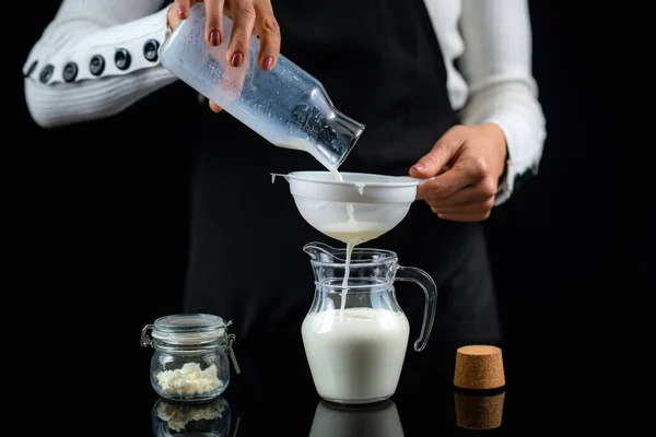 ケフィアの穀物でステイナーを通してミルクを注ぐ 自宅でケフィアを作る女性 — ストック写真